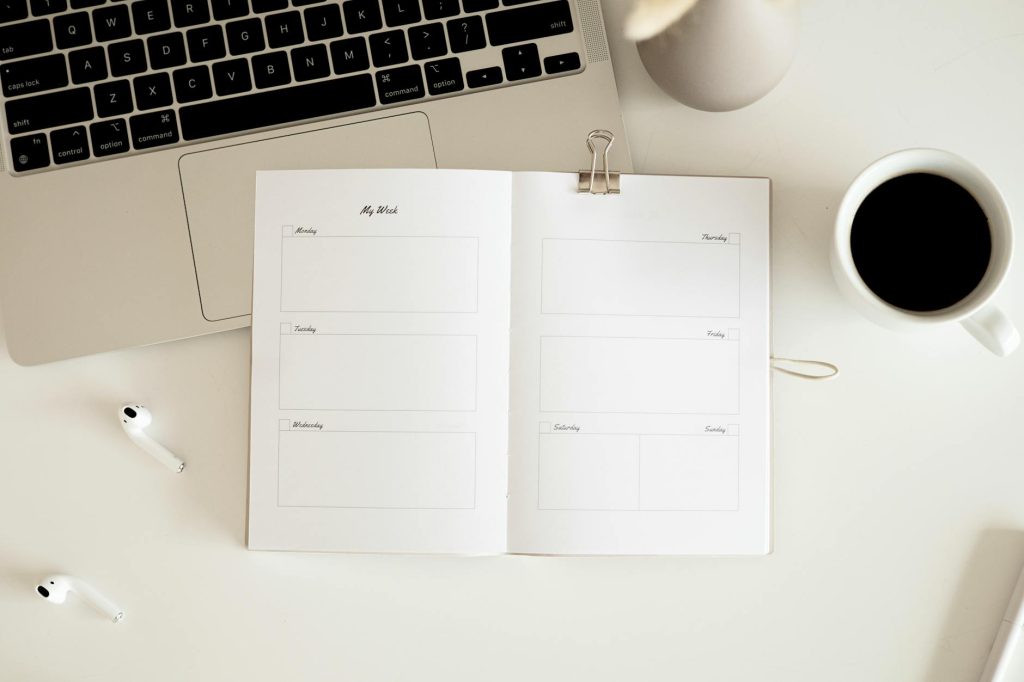 Overhead view of a desk with planner, coffee, laptop, and earbuds in a minimalist style.