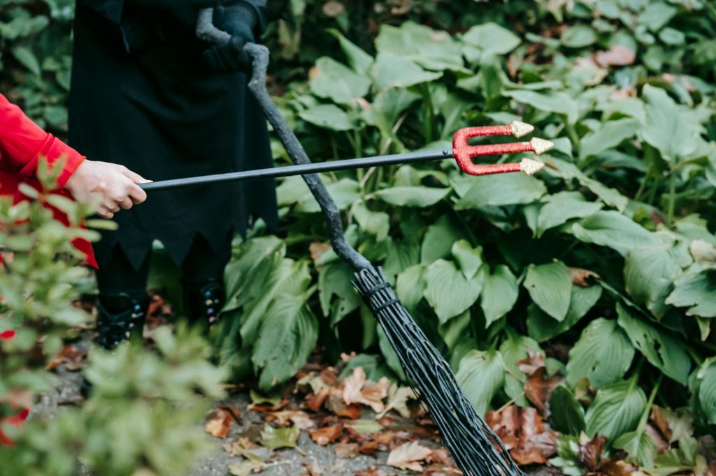 Children playing in Halloween costumes with trident and broom outdoors.