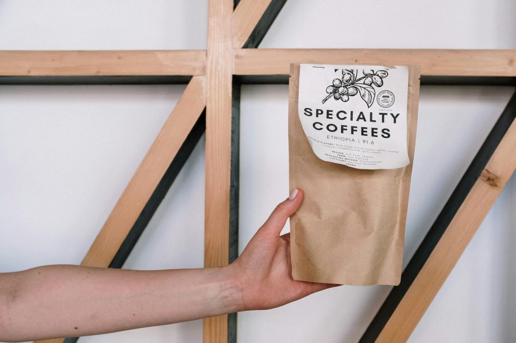 A hand holding a specialty coffee package against a minimalist background with wooden beams.