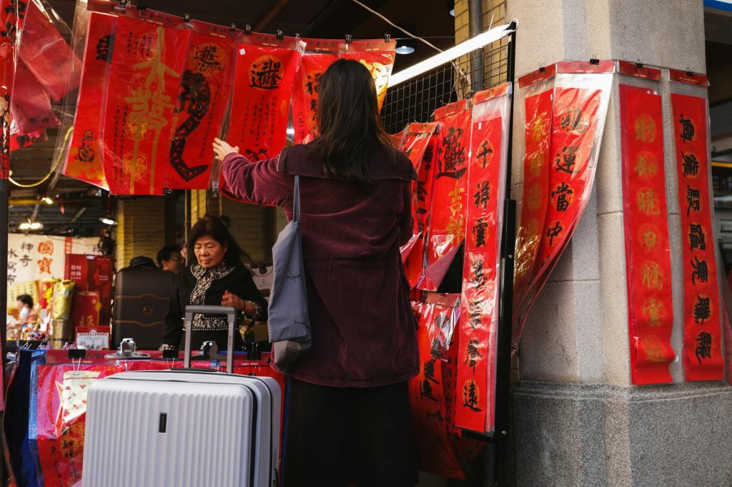 Women shopping at an Asian street market with vibrant red banners during the day.