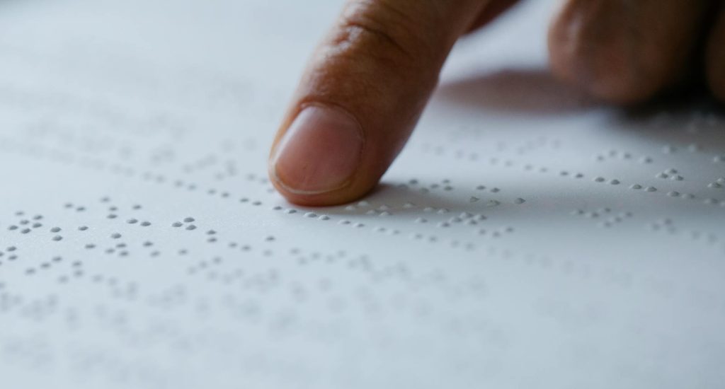 Close-up of a finger reading braille text on a textured white paper, emphasizing touch.