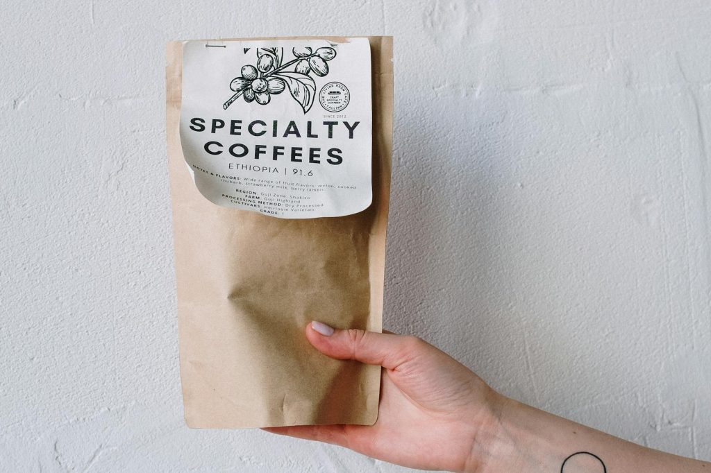 A hand holds a specialty coffee package against a white wall, offering minimalistic and elegant design.