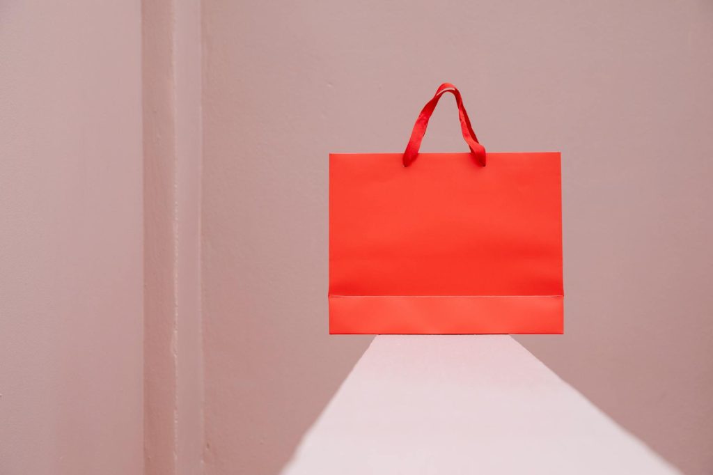 Minimalist image of a red shopping bag against a pink background, perfect for retail themes.