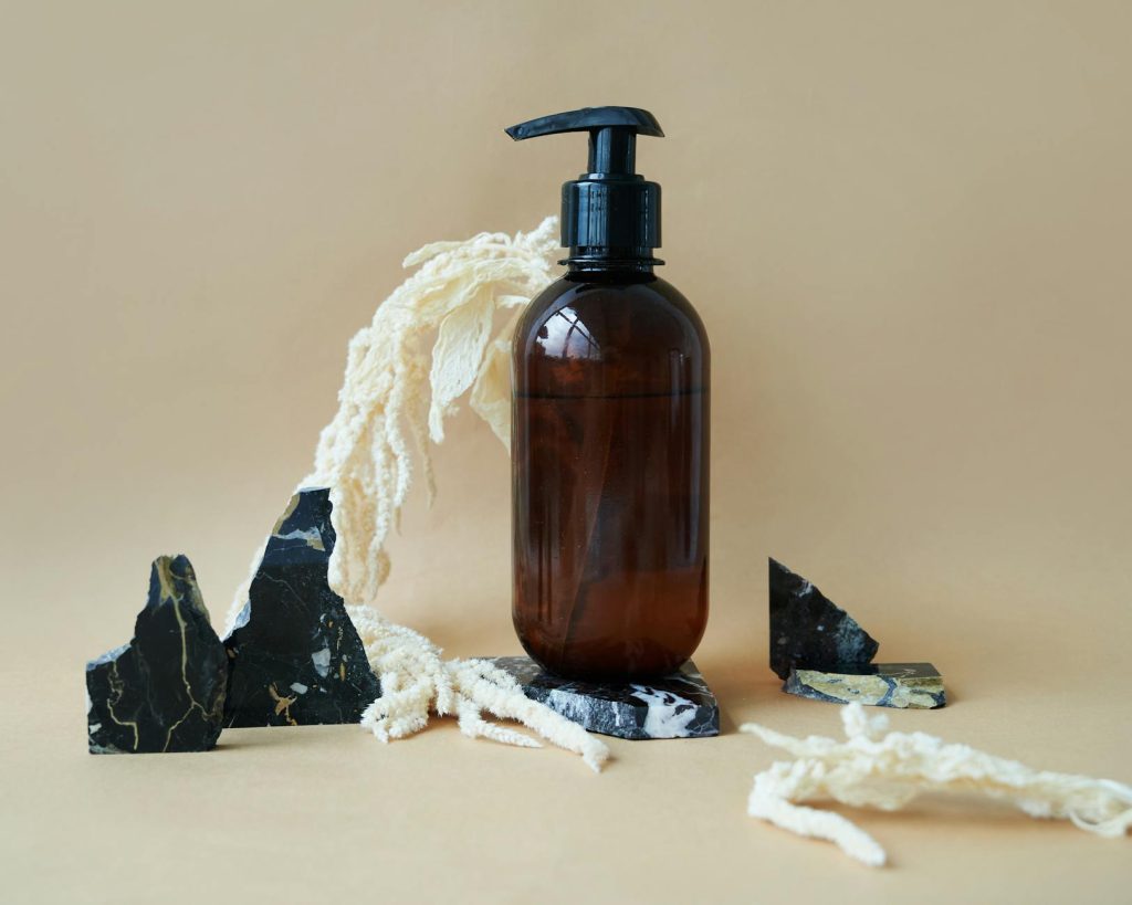 Amber pump bottle surrounded by stones and natural fibers on a neutral background.