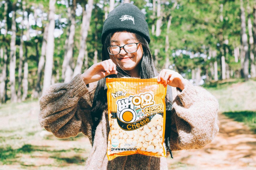Cheerful young woman smiling and holding a cheese snack outdoors in a forest park.