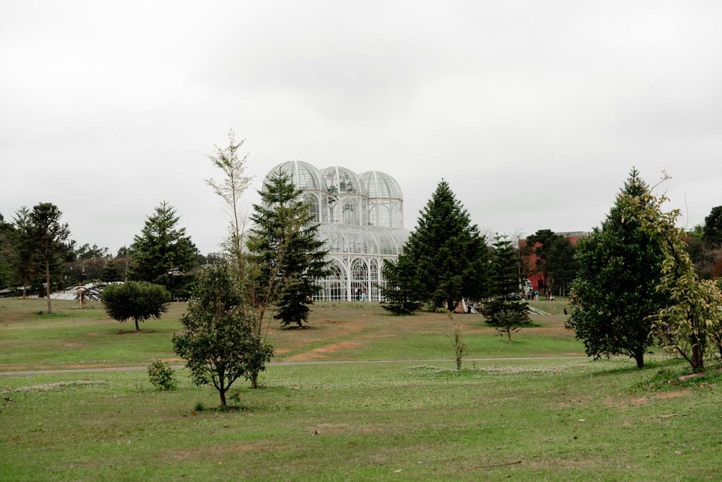 Explore the lush greenery and iconic greenhouse at Curitiba's Botanical Garden on a cloudy day.