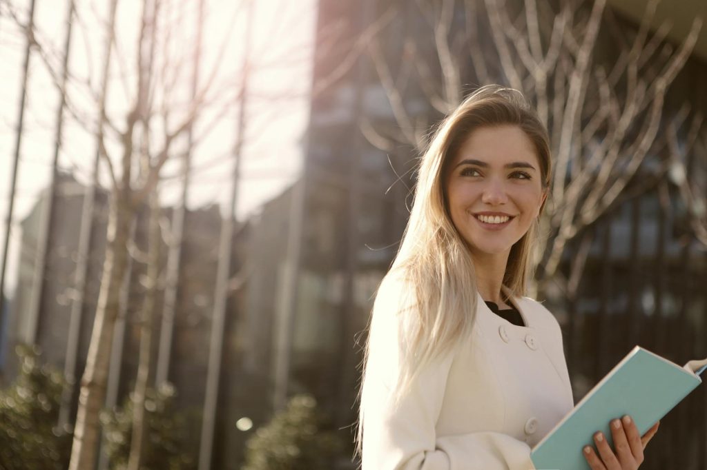 Confident woman smiling with a notebook in outdoor natural light.