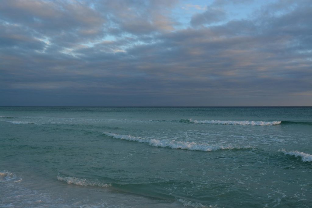 Tranquil view of Destin, Florida beach with gentle waves under a cloudy sky during early morning.