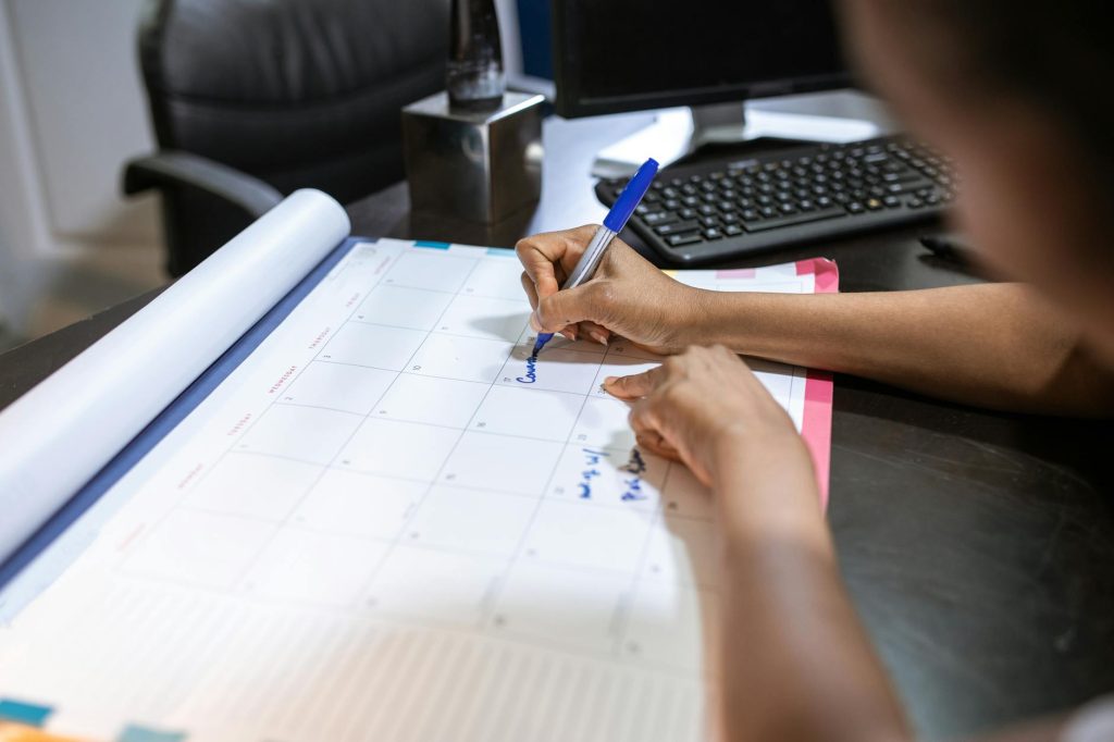 Close-up of a woman planning her schedule on a desk calendar in an office setting.