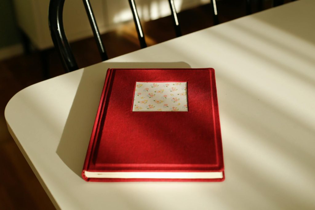 Red journal with flower pattern cover resting on a sunlit white table.