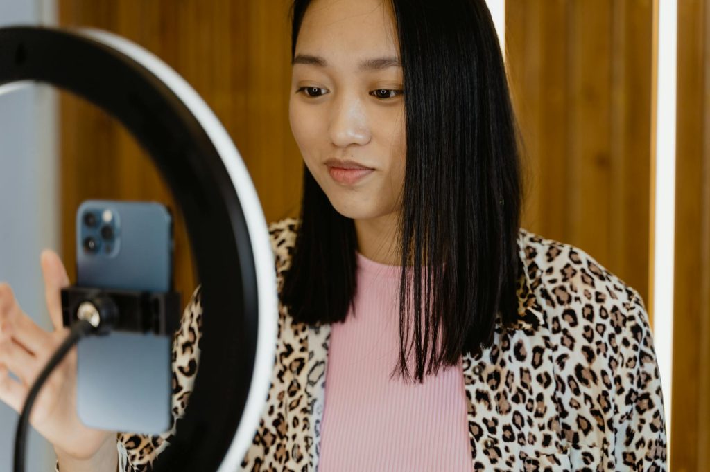 A young woman using a smartphone and ring light for video recording indoors.