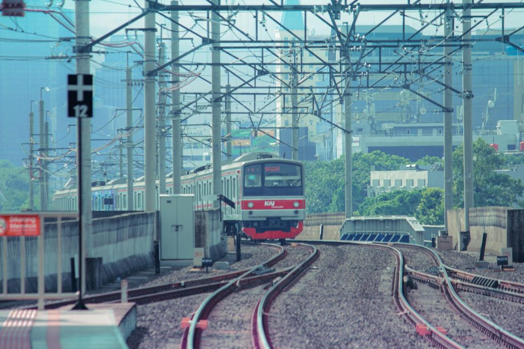 A train approaches a city station on an elevated railway track with urban buildings in the background.