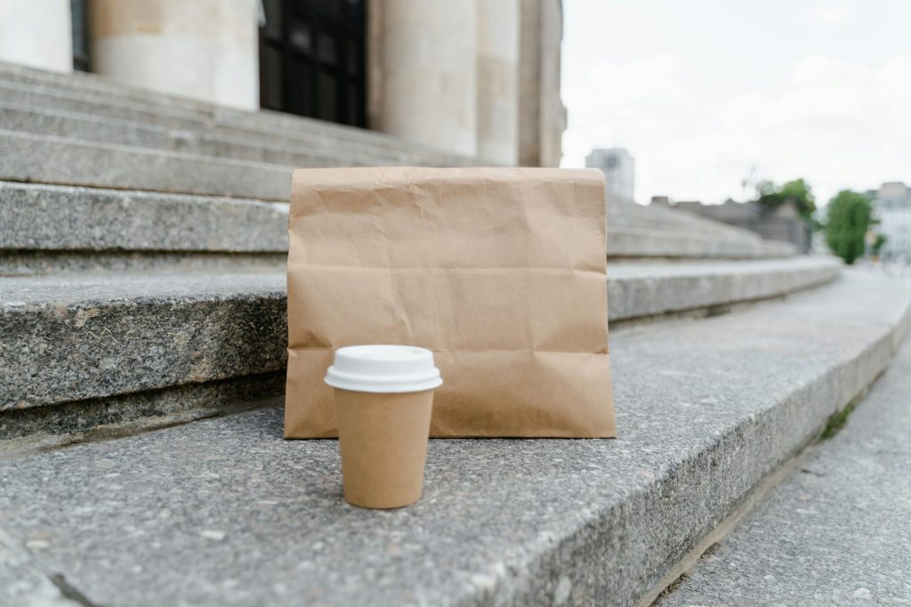 A paper bag with a coffee cup on stone steps in an urban outdoor setting.