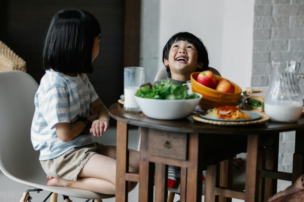 Two happy children enjoying a healthy meal at home, sharing laughter and nutritious food.