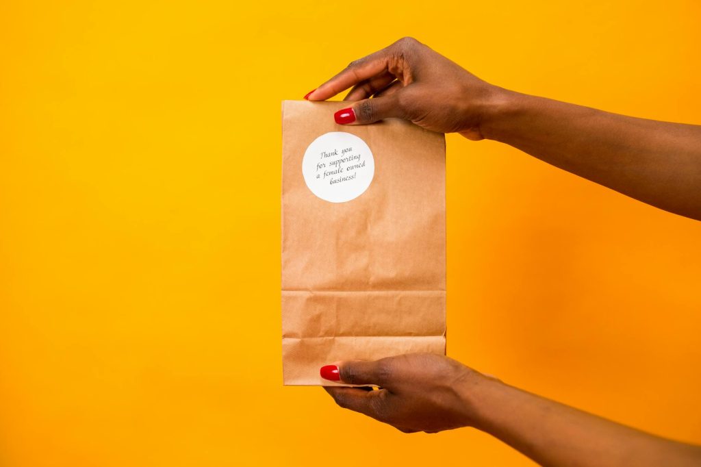 Paper bag with a thank you note held by hands against a vibrant yellow background.