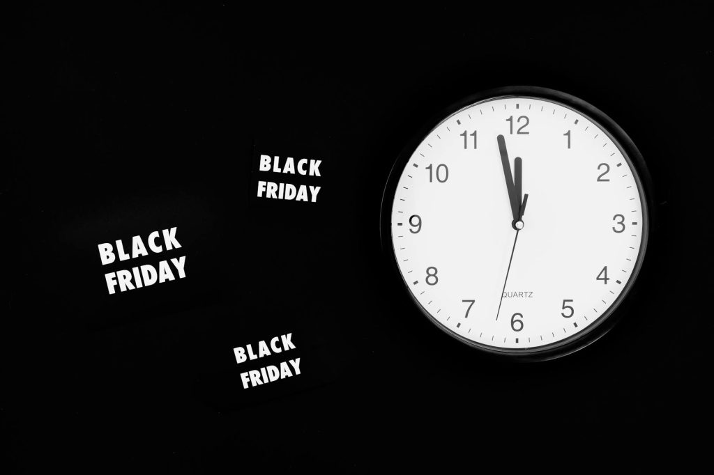 Analogue clock striking midnight for Black Friday sales on a black background.