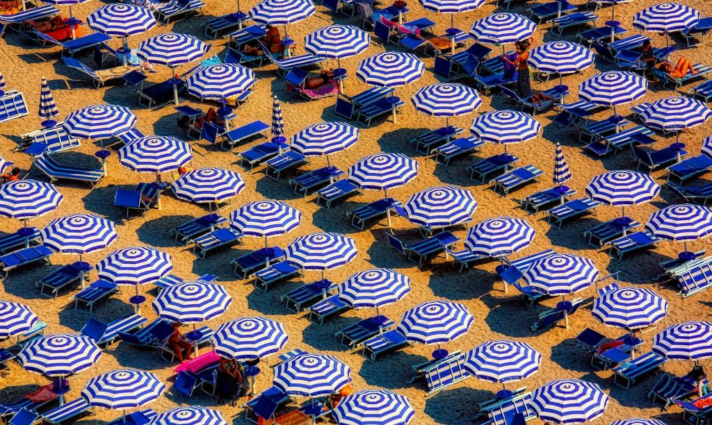 Aerial view of striped blue and white beach umbrellas on a sunny shore.