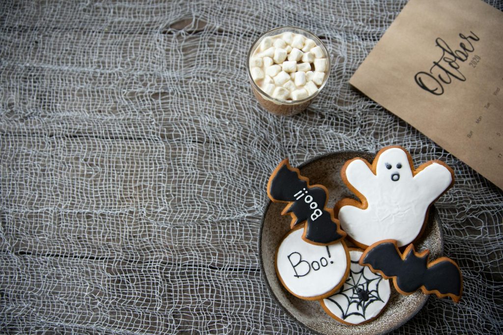Spooky Halloween cookies and hot cocoa on a rustic table with October calendar.