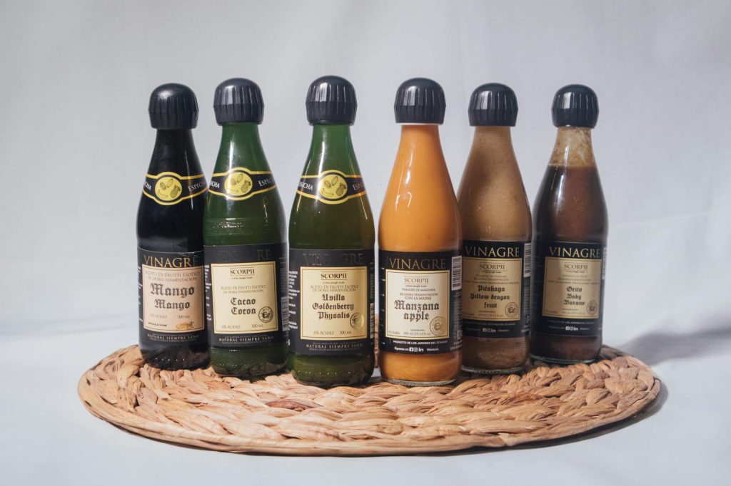 A variety of fruit-flavored vinegar bottles displayed on a woven mat, featuring mango, apple, and more.