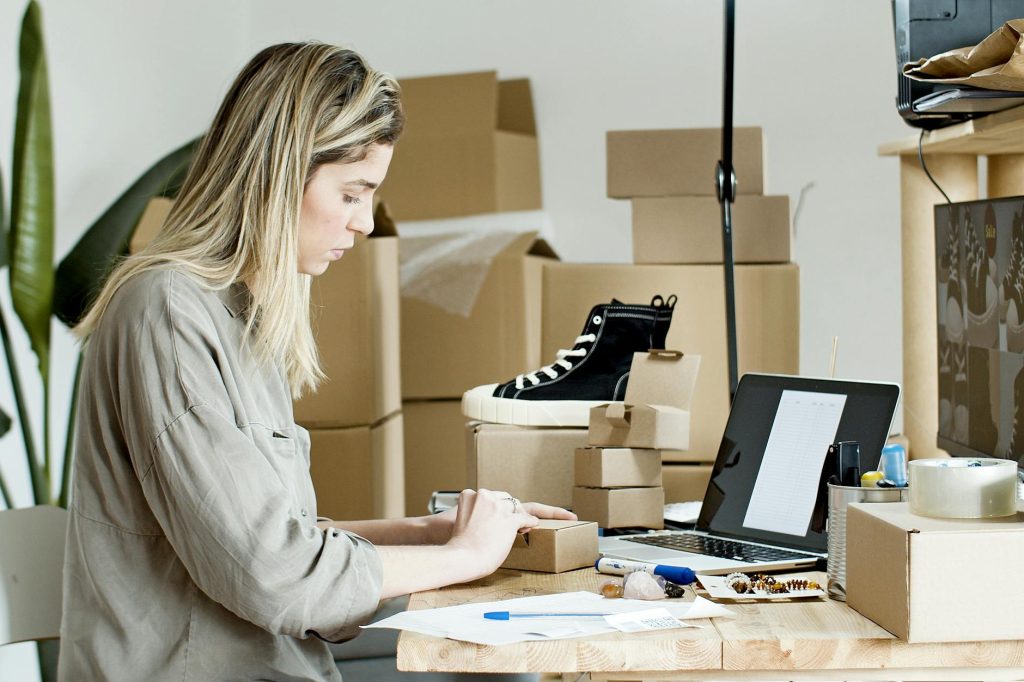 A woman packing boxes for her online store, surrounded by packaging materials and a laptop.
