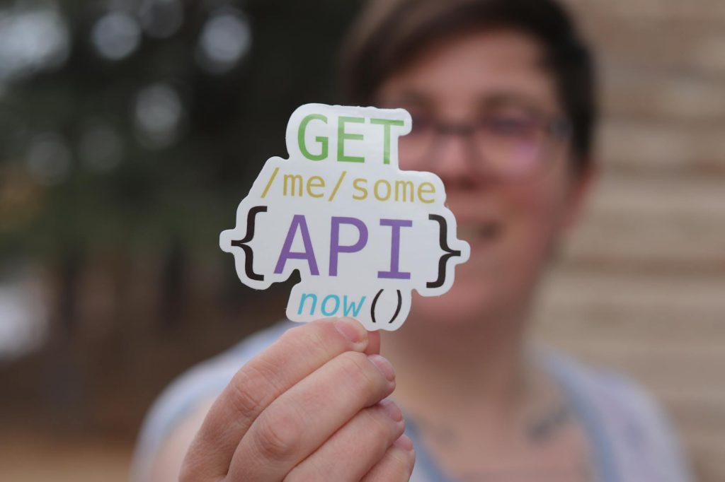 Close-up of a person holding a colorful API-themed sticker with trees blurred in the background.