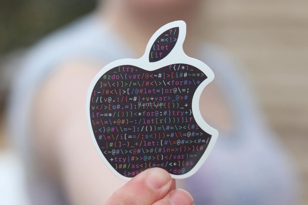 Close-up of a person holding an apple-shaped sticker with binary code, symbolizing technology.