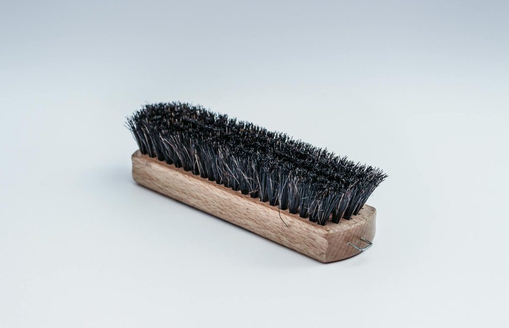 Close-up of a wooden cleaning brush with dense black bristles on a white background.