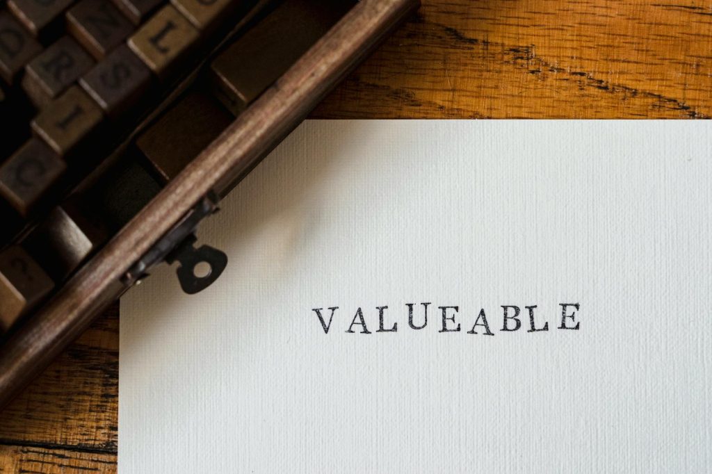 A classic typewriter typing 'VALUEABLE' on a white sheet on a wooden table.