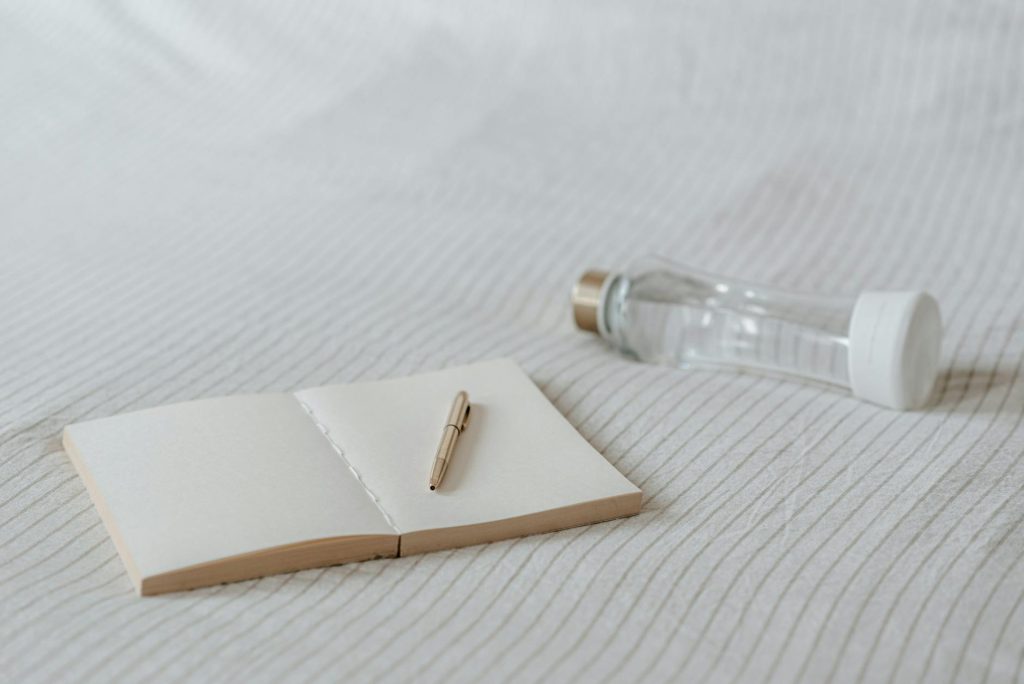A cozy minimalistic setup featuring a notebook and a water bottle on a bed. Perfect for living space inspirations.