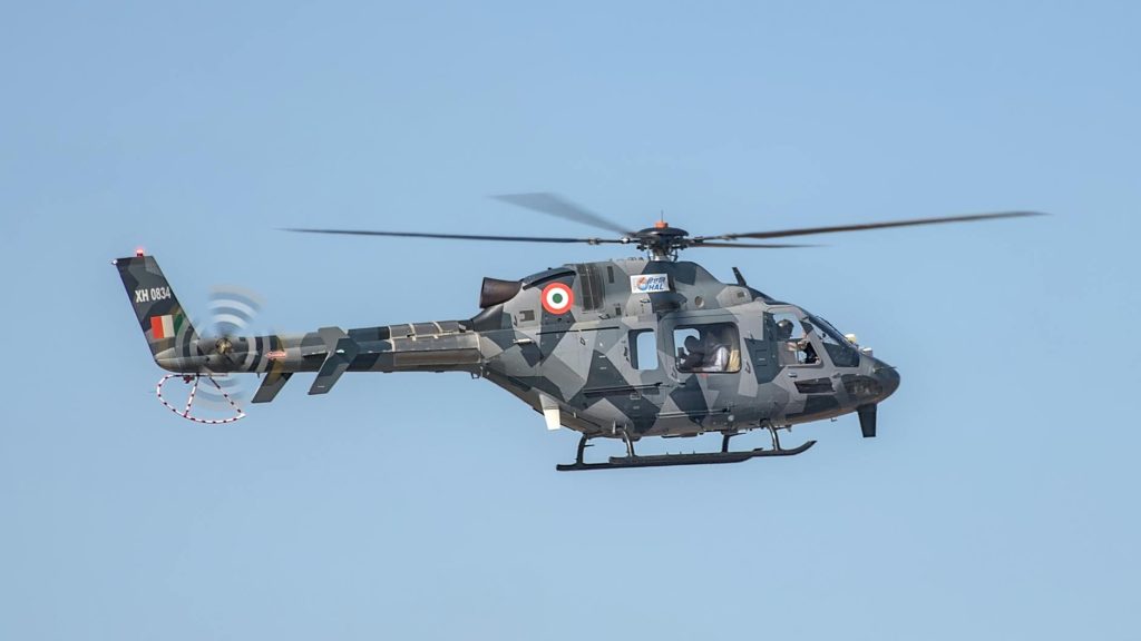 A military helicopter in flight at Aero India, Bengaluru, clear blue sky.