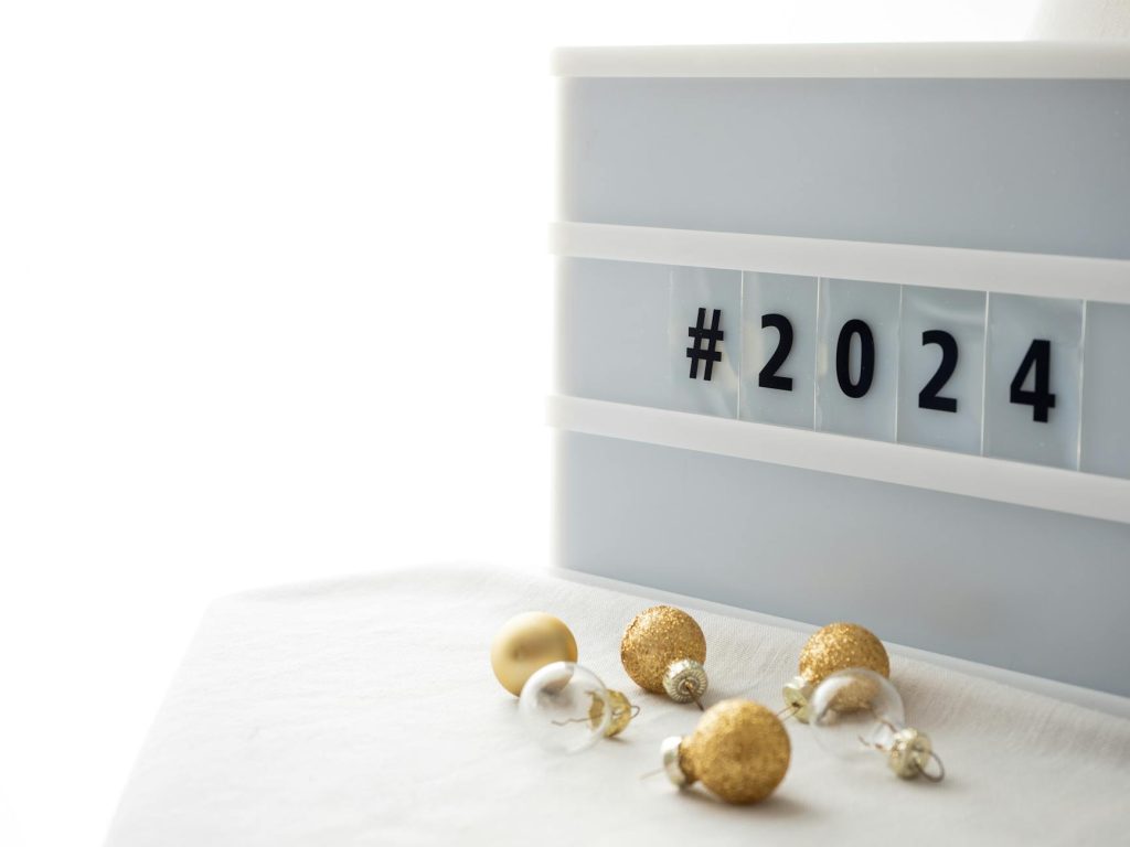 Elegant 2024 New Year setup with hashtag and gold baubles on white background.
