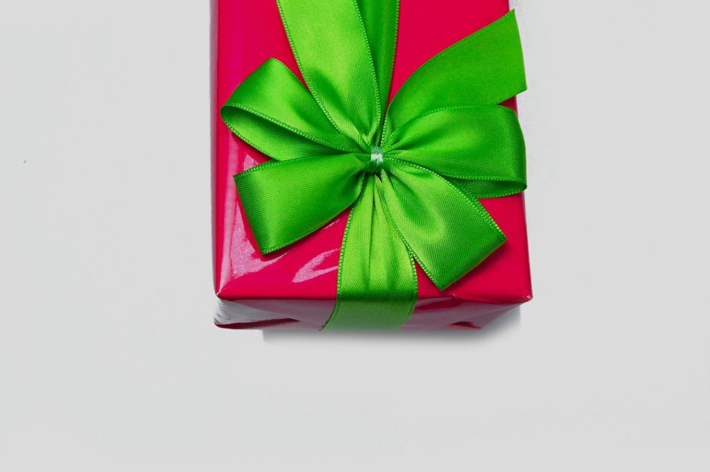 A bright red gift wrapped in a glossy paper with an elegant green ribbon bow.