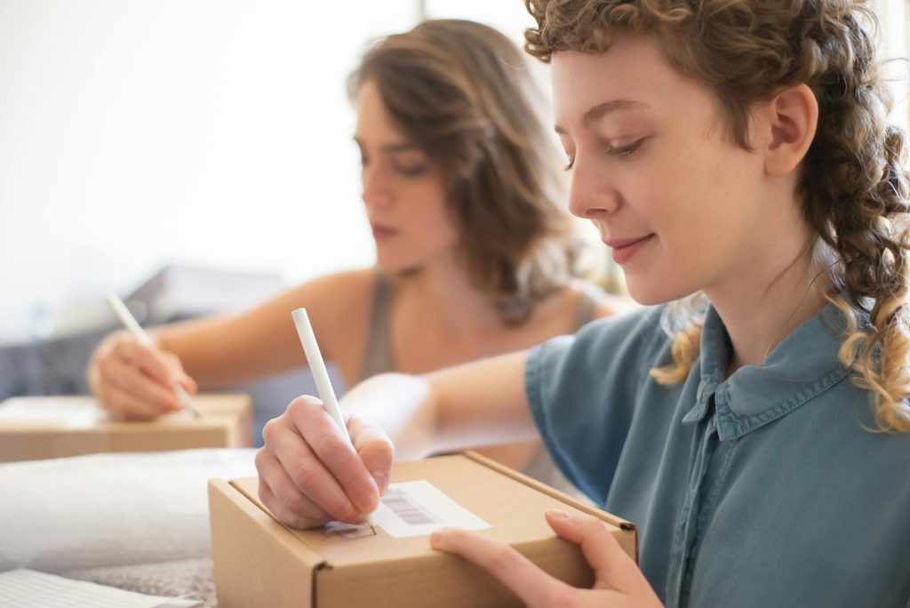 Two women packing boxes for an online store, focusing on barcode and labeling processes.
