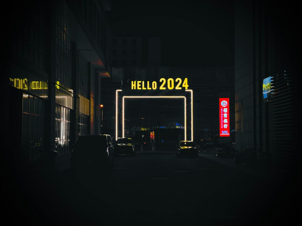 Urban night scene features an illuminated 'Hello 2024' sign in a bustling city alleyway.