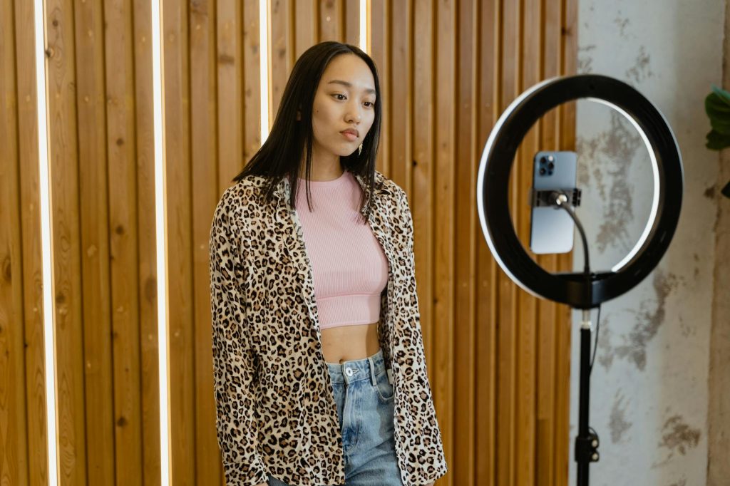 Asian female influencer recording content with ring light and smartphone indoors.