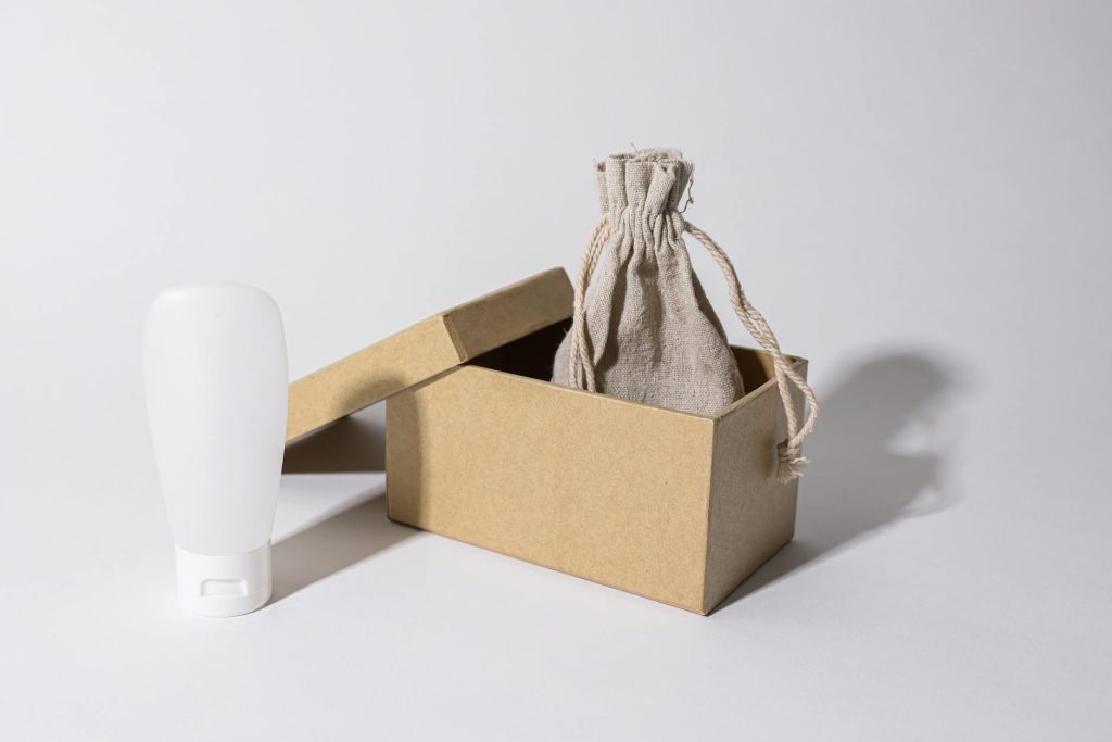 Minimalist photo of eco-friendly packaging with a cardboard box, pouch, and white plastic bottle.
