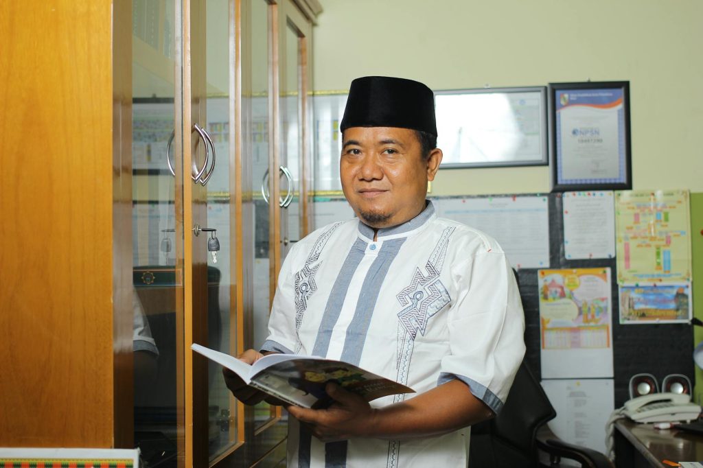 A teacher standing in an office in Indonesia, holding a book, conveying education.