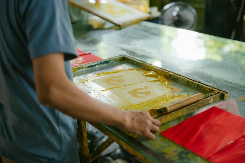 Artisan crafting screen prints indoors, showcasing creativity and skill in handmade art production.