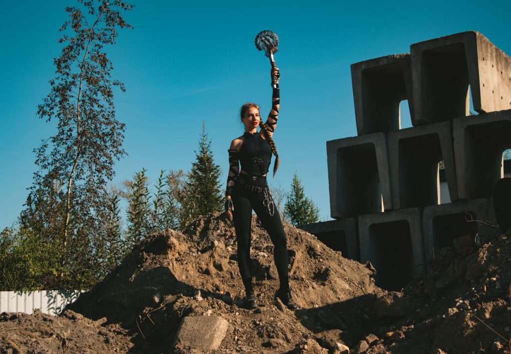 A strong female warrior character stands confidently holding a weapon in a construction site setting.