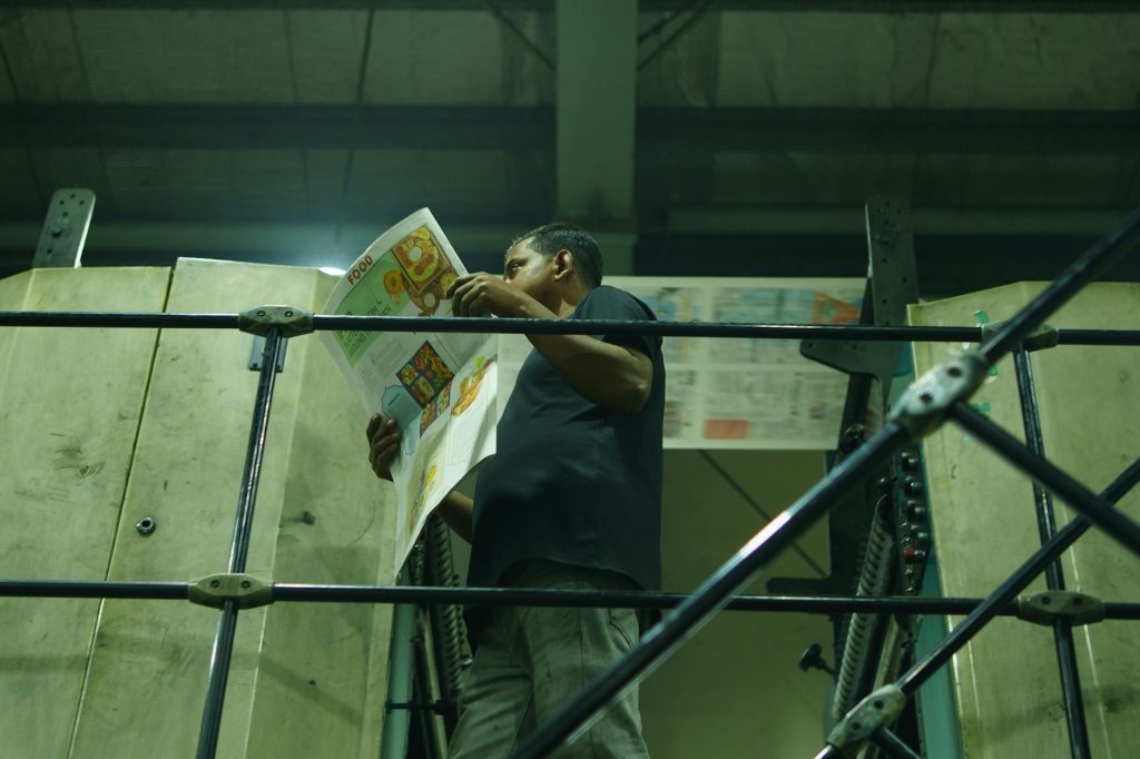 Man examines printed newspaper in an industrial printing environment with machinery.