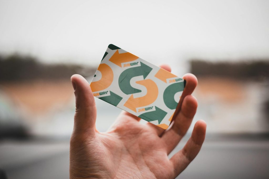 A hand holding a colorful gift card with arrows and text against a blurred background.