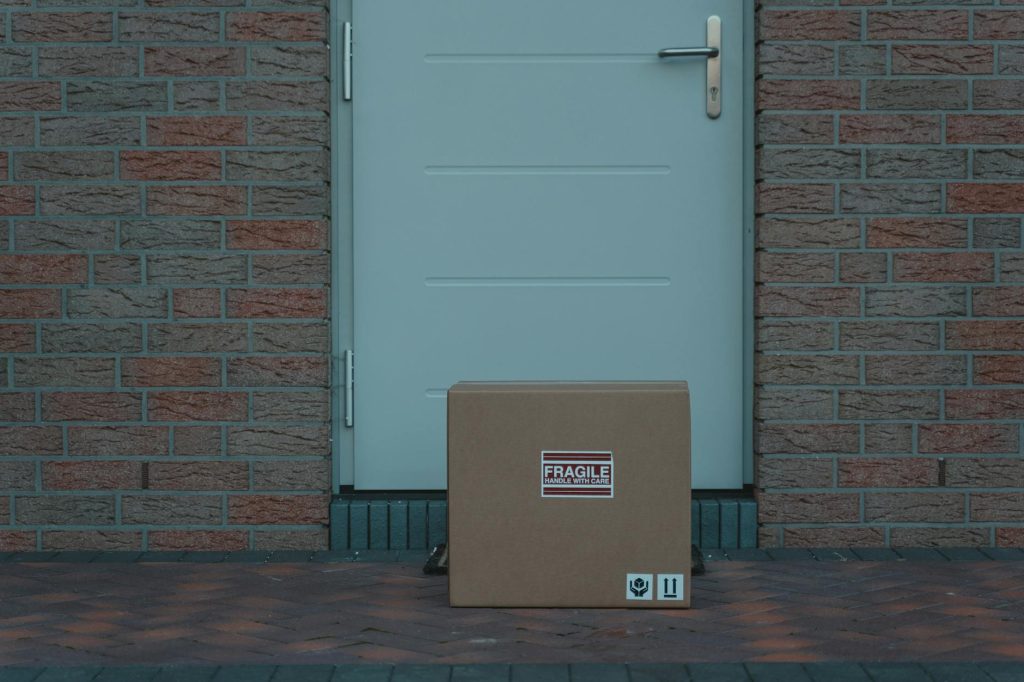 Cardboard box placed outside a brick-walled entrance, labeled fragile for delivery.