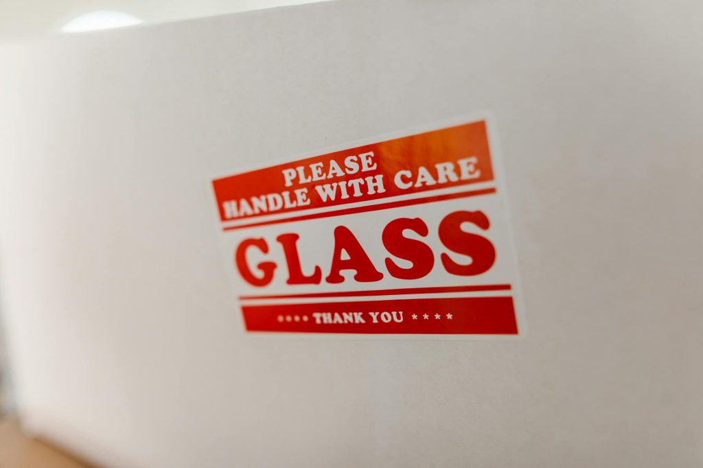 Close-up of a glass packaging label with 'Handle with Care' warning text on a white box.