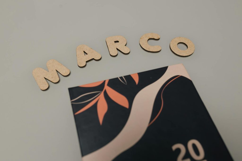 Wooden letters spelling 'MARCO' arranged above an artistic notebook on a light surface.