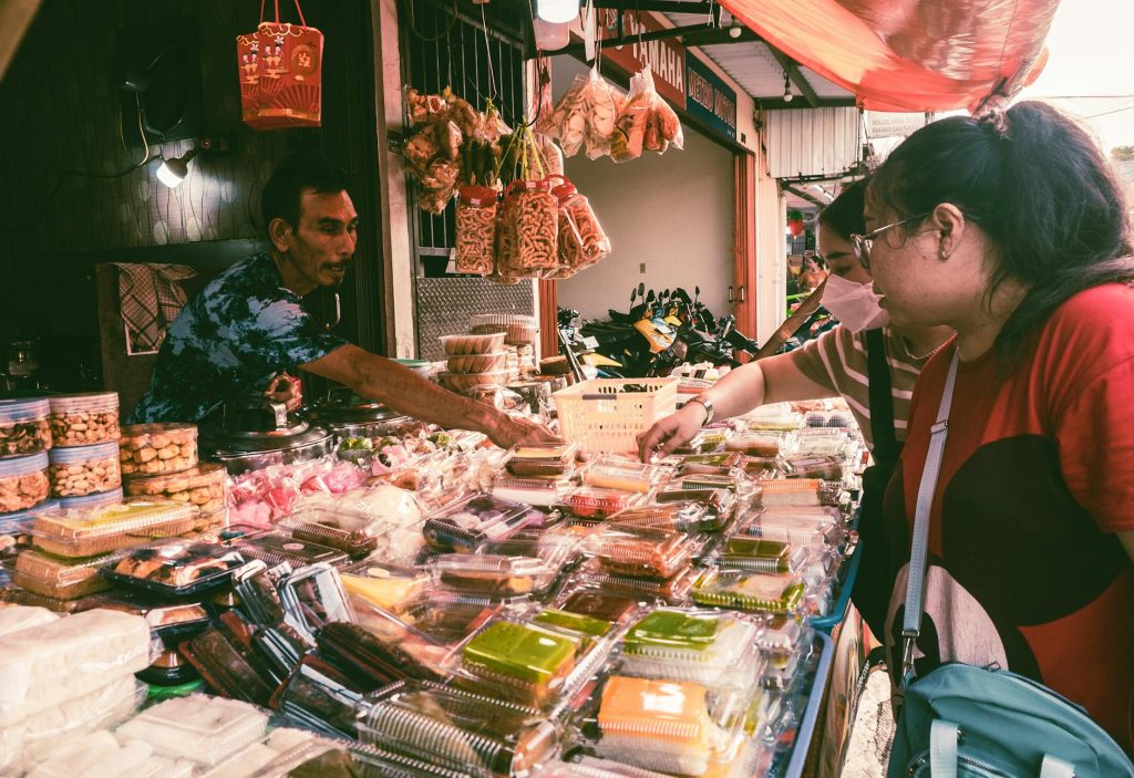 Market scene with customers buying various snacks from a vendor, vibrant setting.