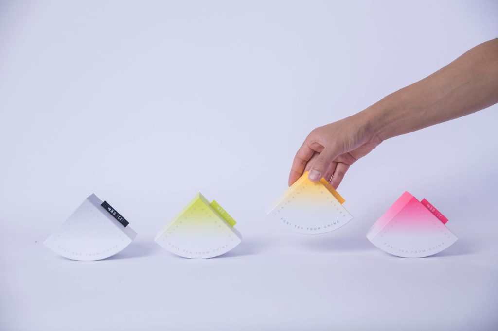 Colorful pyramid-shaped tea packaging showcased in a minimalist setup with a hand interaction.