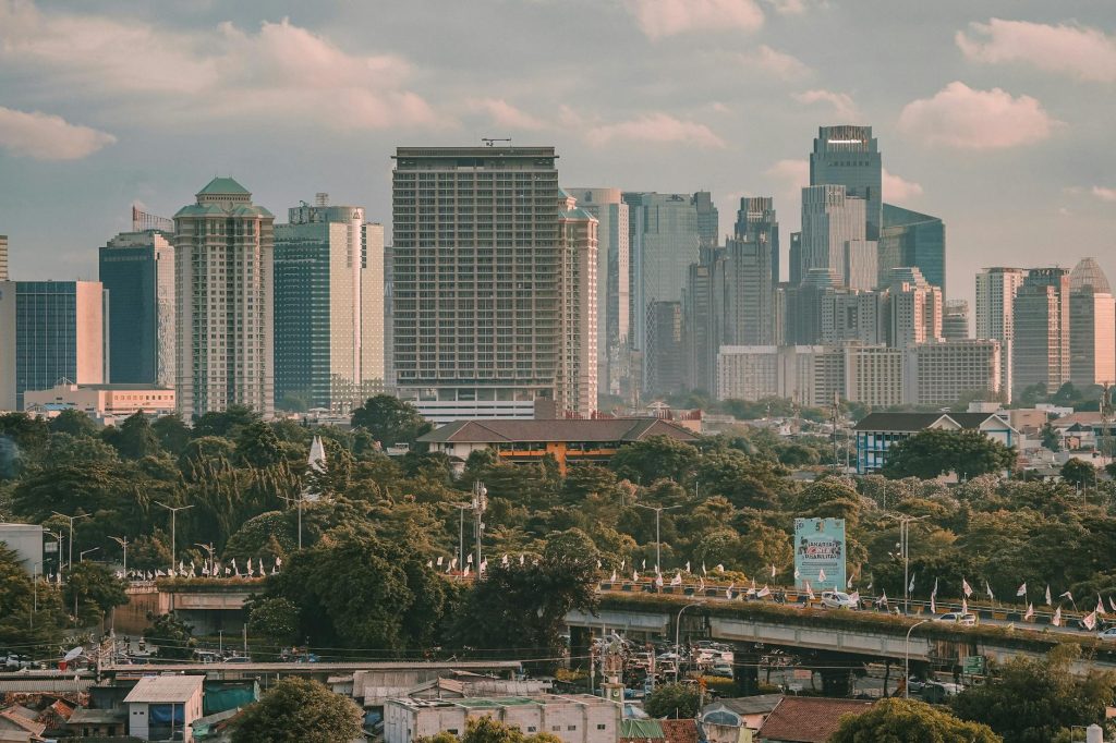 Aerial view of Jakarta's skyline showcasing modern skyscrapers and lush greenery under a cloudy sky.