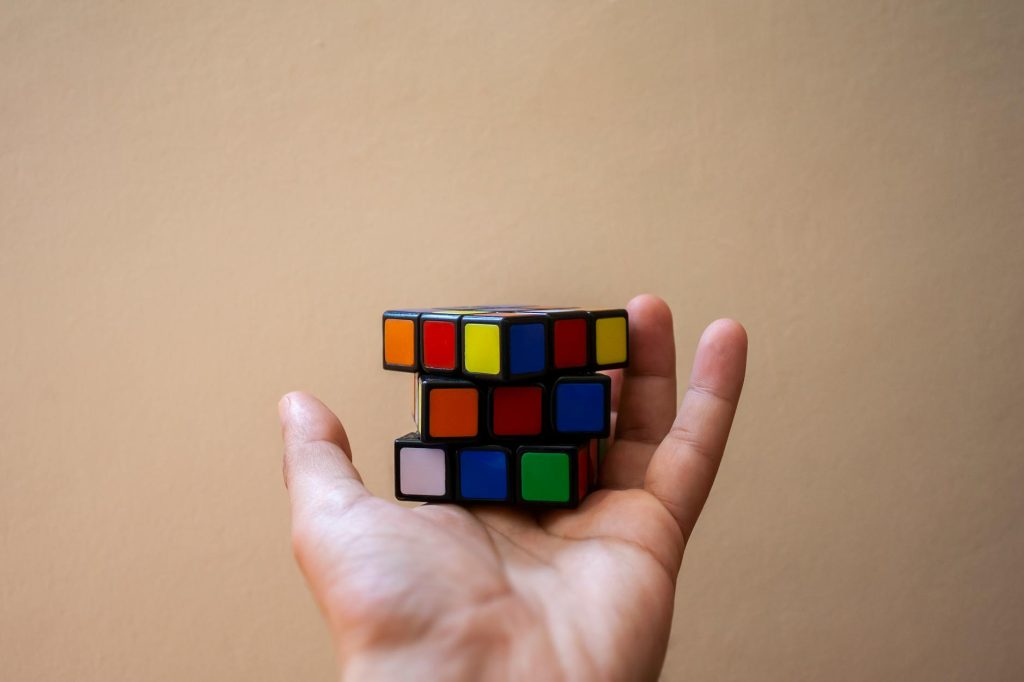 Close-up of a hand holding a colorful Rubik's Cube against a plain background.