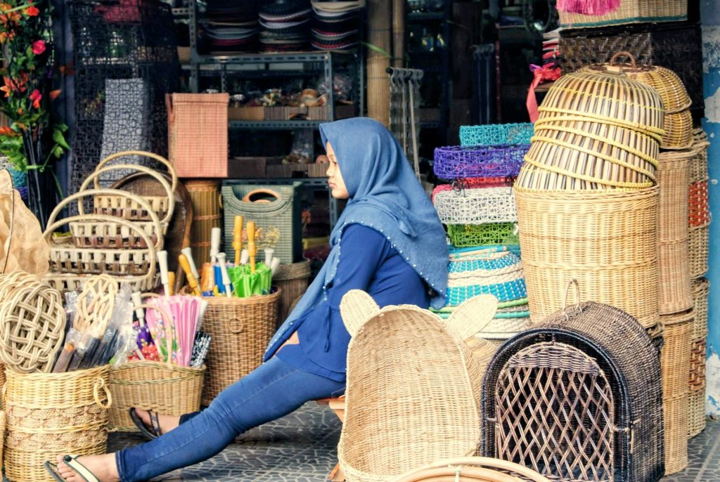 Woman in hijab sitting by baskets at traditional market in Tasikmalaya, Indonesia.