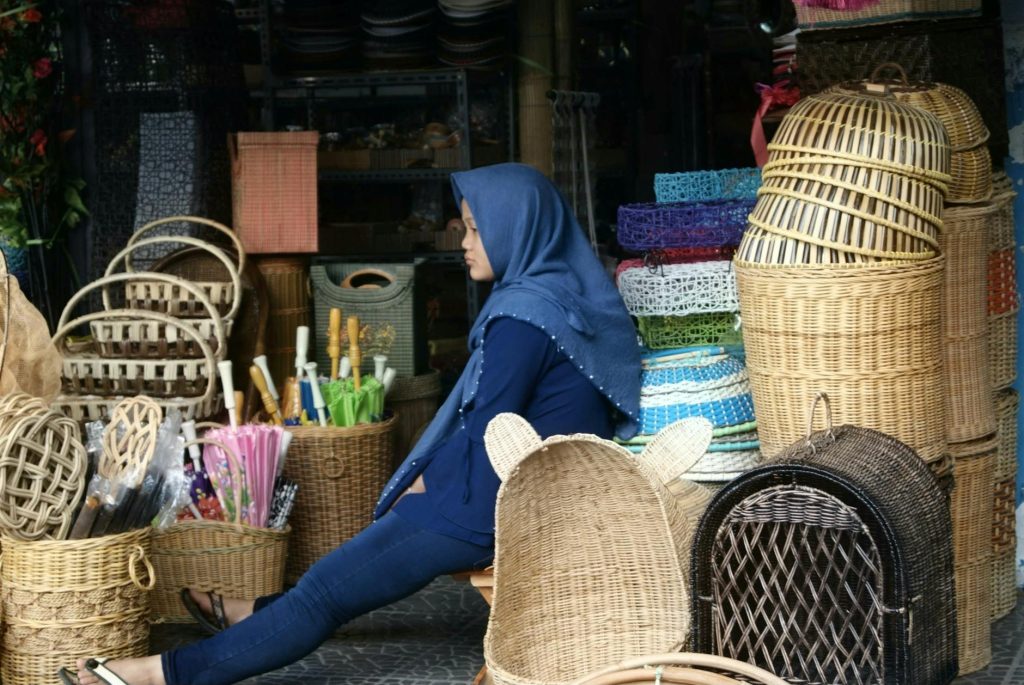 Woman in Tasikmalaya market surrounded by colorful traditional woven baskets.